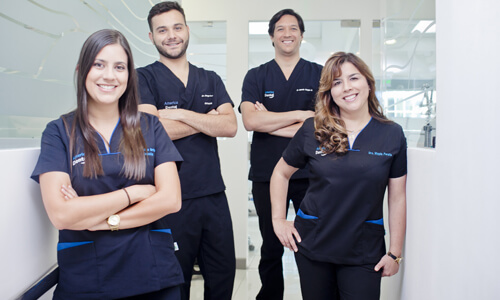 Picture of a dental team representing the dental services of the Costa Rica Dental Center in San Jose, Costa Rica. The team consists of 2 male dentists and 2 female dentists, who are wearing dark blue work uniforms.