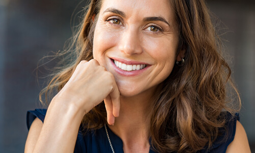 Picture of a smiling woman, happy with the cosmetic dental treatments she had at the Costa Rica Dental Center in San Jose, Costa Rica. The woman has long brown hair and is wearing a black blouse. She has perfect teeth and is smiling directly at the camera.